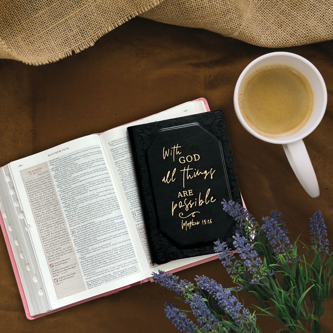 Bible open to the Book of Matthew with a black journal titled 'With God All Things Are Possible' resting on top, alongside a cup of coffee and lavender flowers, creating a peaceful devotional setting.