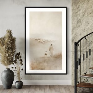 A beautifully framed biblical art print featuring Jesus as the Good Shepherd walking through a misty field, leading a flock of sheep. The minimalist sepia-toned artwork emphasizes the serene and symbolic imagery of Jesus guiding a single lamb, with the rest of the flock in the distance. This fine art print is displayed in a modern, neutral-toned living room with natural wood floors, a spiral staircase, and decorative pampas grass arrangements in ceramic vases, creating a peaceful and elegant atmosphere.
